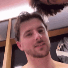 a shirtless man with a beard looks at the camera