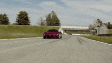 a red car is driving down a road with a bridge in the background