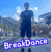 a man wearing sunglasses and a guess shirt stands in front of a fence with the words break dance written on the ground
