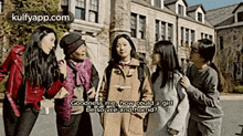 a group of women are standing next to each other in front of a building and talking .