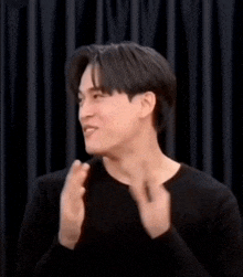 a young man in a black shirt is laughing and clapping his hands .