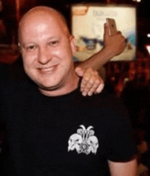 a bald man in a black shirt is taking a picture of himself with a cell phone .