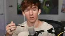 a man wearing ear buds is holding a spoon in front of a microphone .
