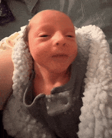 a baby is wrapped in a white blanket and looks at the camera