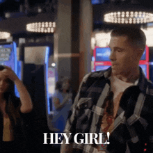 a man in a plaid shirt stands in front of a woman and says hey girl