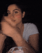 a woman in a white t-shirt is sitting at a table in the dark