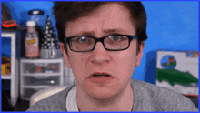a man wearing glasses and a grey sweater is making a funny face