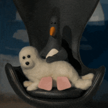 a stuffed seal and a stuffed penguin are sitting on a black chair