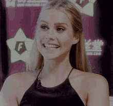 a woman in a black top is smiling in front of a sign that says ' f ' on it .