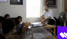 a group of people are sitting around a table with a fan
