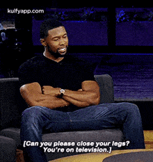 a man is sitting in a chair with his legs crossed and laughing while talking about television .