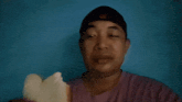 a man wearing a hat and a purple shirt is eating a piece of bread