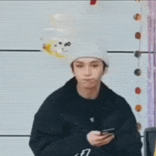 a man wearing a beanie and a black jacket is holding a cell phone in his hand .