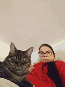 a woman wearing glasses and a red sweater is laying next to a cat
