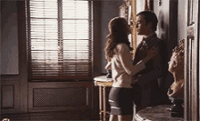 a man and a woman are kissing in a room with a window .