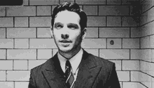 a man in a suit and tie standing in front of a brick wall