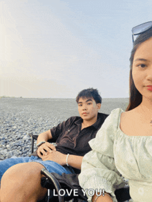 a man and a woman sitting on a rocky beach with the words i love you