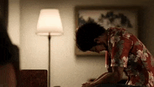 a man in a hawaiian shirt is sitting on a bed with his head down in a dark room .