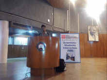 a man stands behind a podium in front of a sign that says scientists students interaction