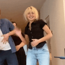 a woman in a black shirt and blue jeans is dancing with a man