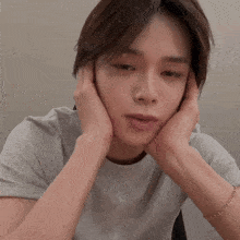 a man with his hands on his face is wearing a grey shirt