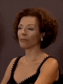 a woman with curly hair is wearing a black top and pearl earrings .