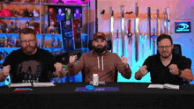 three men are sitting at a table and one has an avatar shirt on