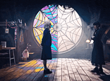 two women stand in front of a stained glass window with a spider web design