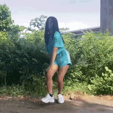 a woman in a blue shirt and shorts is dancing on the side of a road