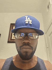 a man wearing glasses and a blue la hat looks at the camera