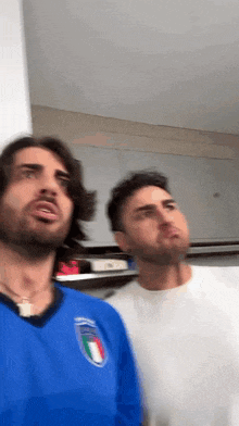 two men are standing next to each other and one of them is wearing a blue shirt with the italian flag on it