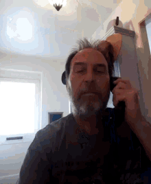 a man with a beard is talking on a cell phone with his eyes closed