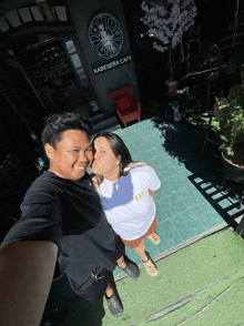 a man kissing a woman in front of a kabesara cafe