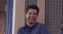 a man in a blue shirt is standing in front of a window with his mouth wide open .