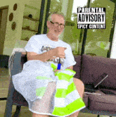 a man is sitting in a chair with a parental advisory sticker on his shirt
