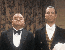 two men in tuxedos stand next to each other