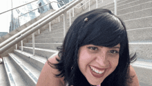 a woman with black hair smiles in front of stairs