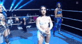 a group of women are standing in a wrestling ring with a referee in the background .