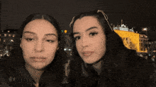 two women are standing next to each other in front of a building that has a yellow light on it