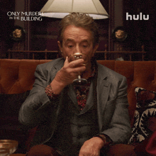 a man sitting on a couch drinking from a glass with a hulu ad behind him