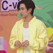 a man wearing a yellow jacket and a white tank top is standing in front of a microphone .