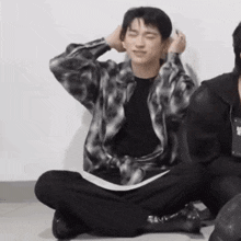 a man in a plaid shirt is sitting on the floor with his hands on his head