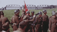a group of soldiers are gathered in a field with a red flag in the background