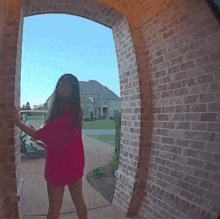 a woman in a red shirt is standing in front of a brick archway