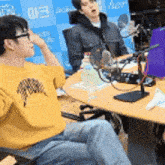 a man wearing a yellow shirt is sitting at a table with a microphone in front of him .