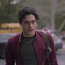 a young man with curly hair is wearing a red shirt and a green sweater .