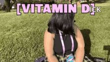 a woman is sitting on the grass in a park with the words `` vitamin dick '' written above her .