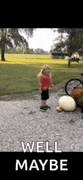 a little girl is standing next to a large pumpkin in a yard .