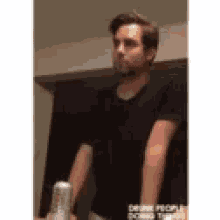 a man in a black shirt is standing in front of a mirror holding a can of beer .