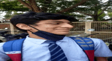 a boy wearing a mask and a skybags backpack stands in front of a fence